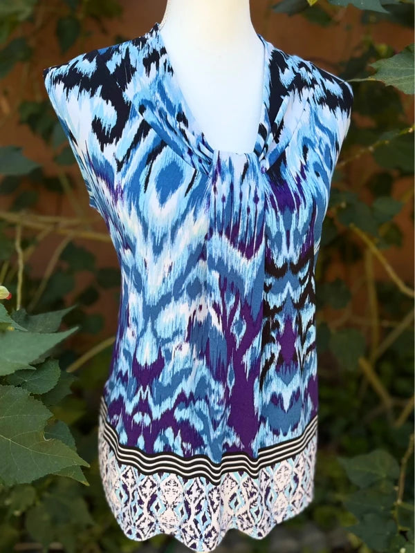 Dana Buchman sleeveless with a blue, purple, black, and white geometric pattern, displayed on a white mannequin torso with green foliage in the background.