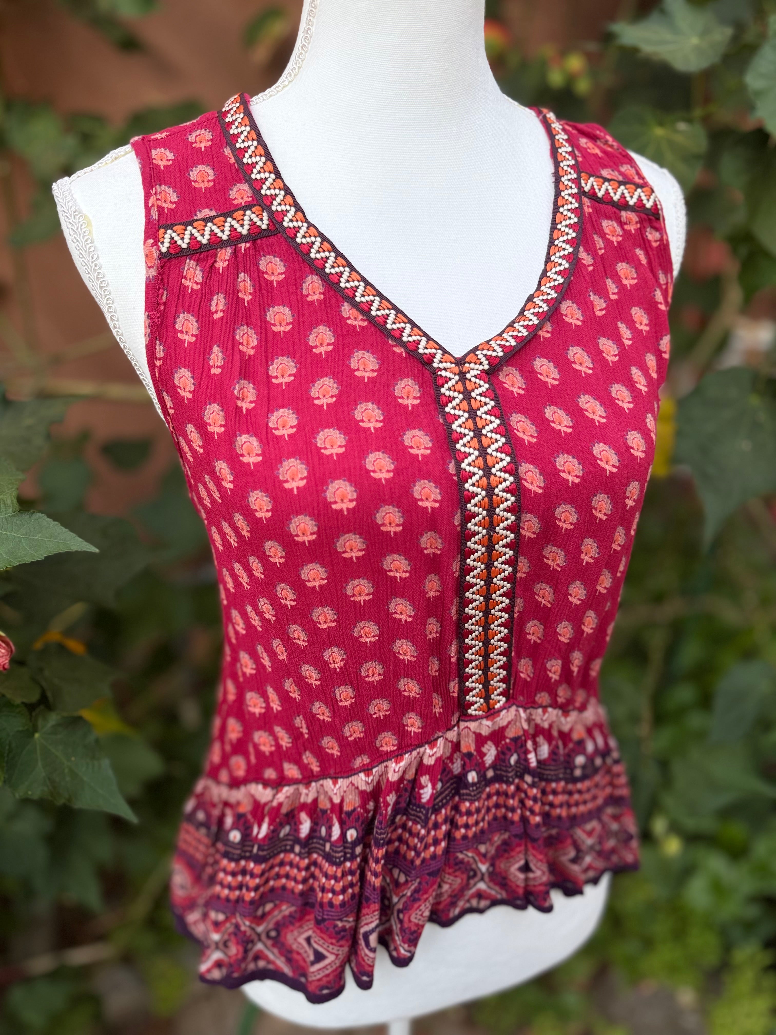 A sleeveless red top with a small floral print, geometric trim, and a ruffled hem.